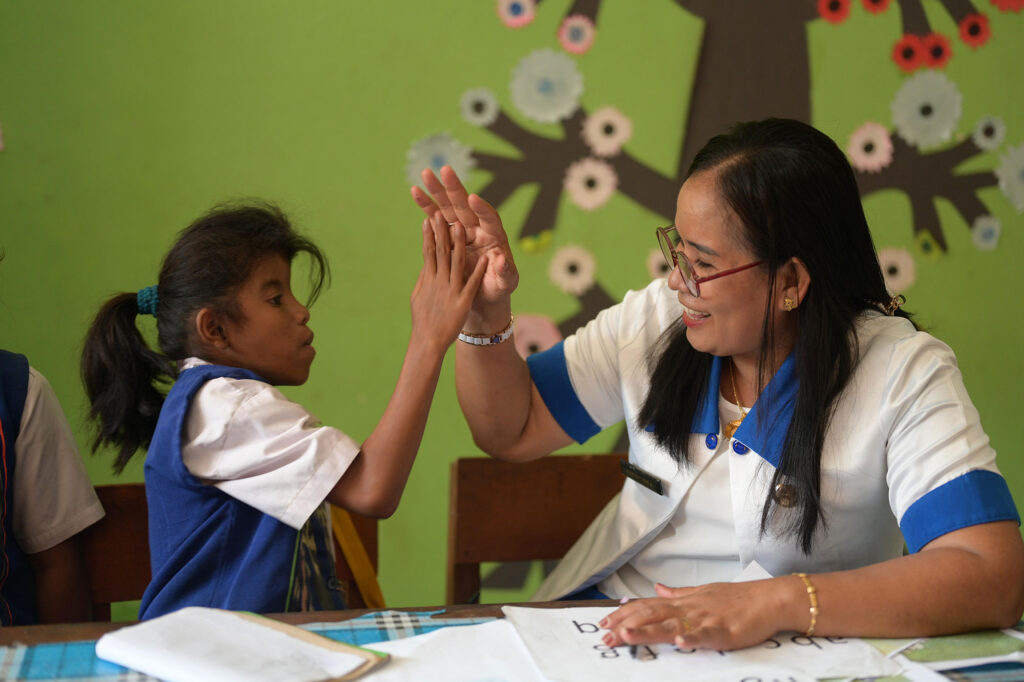 Seorang guru sekolah inklusif mendampingi anak berkebutuhan khusus belajar membaca.